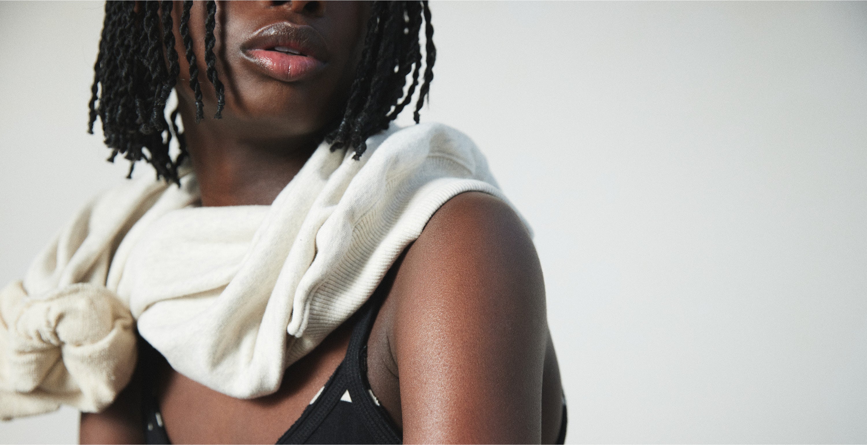 Close-up of woman wearing a black and white top and soft white melee sweater over her shoulders.