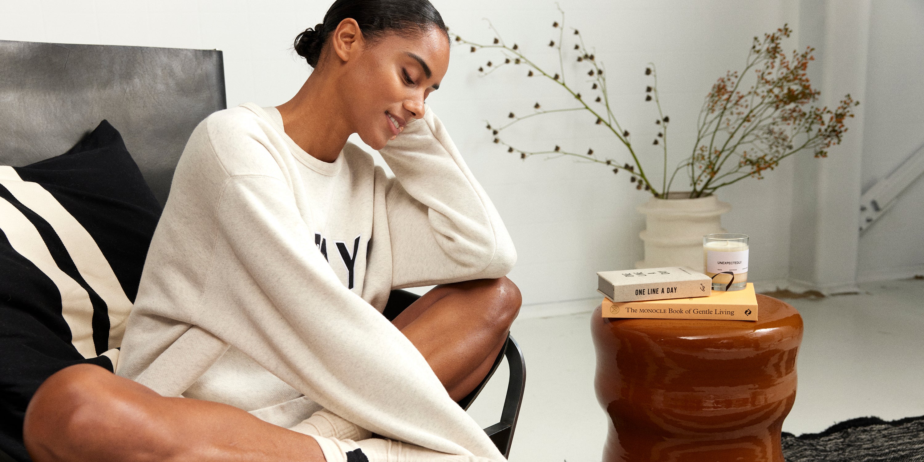 Woman sitting in chair, wearing a soft white melee statement sweater. 